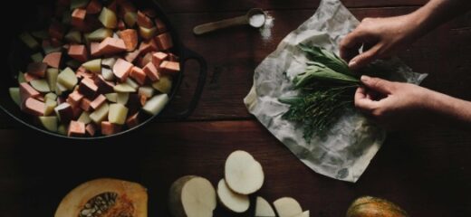 An image shows a person's hand putting some green herbs on Abeego's wrapping paper and some chopped vegetables placed on the table.