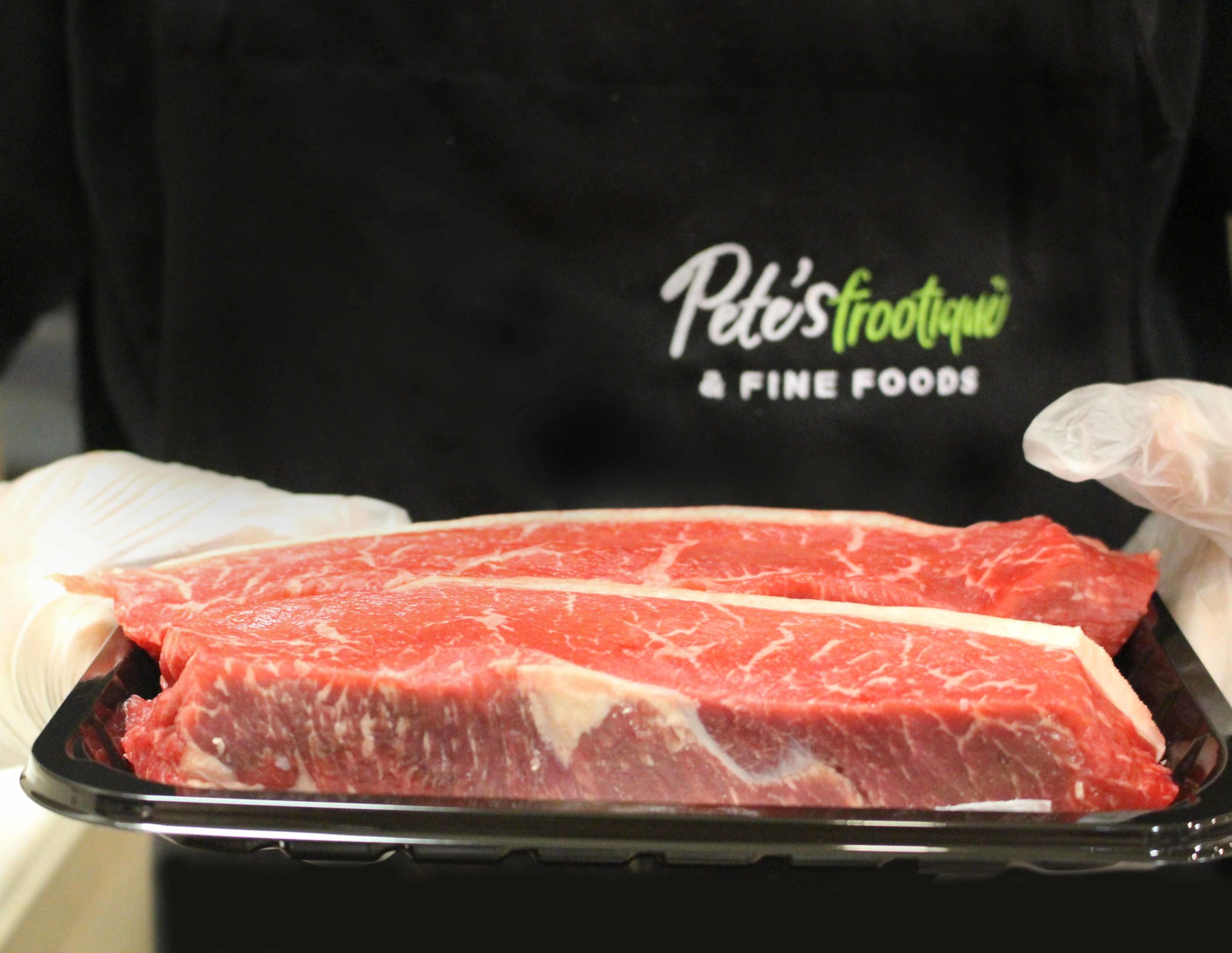 A person in a Pete's Frootique uniform holds a package of beef in front of the camera.