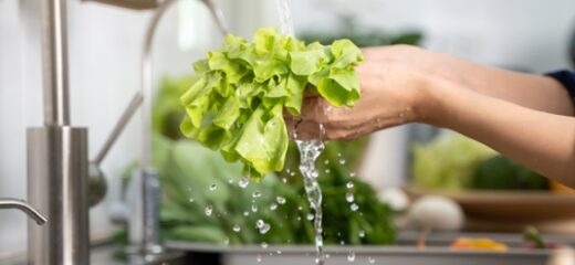 A picture of a person washing green leaves in the sink of the Kitchen.