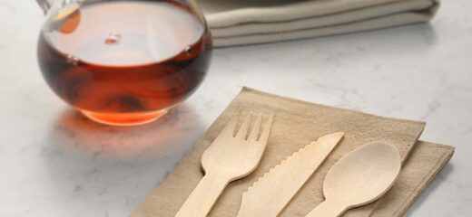 An image shows a wooden fork, spoon, and knife placed on a handkerchief, along with a glass container filled with honey & pancakes placed on a plate.