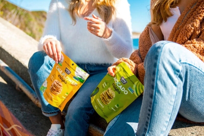 A picture of two girls sitting outdoors and holding Hippi snacks packet in their hands.