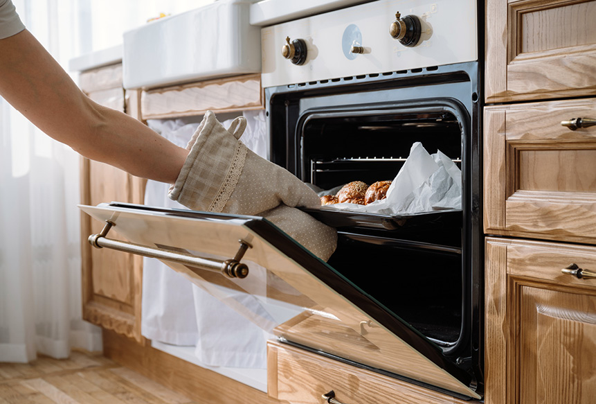Woman taking bread rolls out of the oven