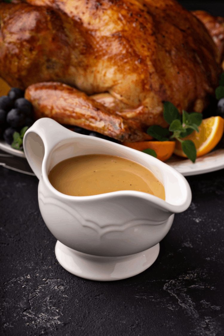 Turkey gravy in white gravy boat with roasted whole turkey in background